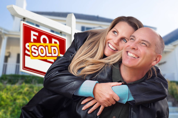 Pareja feliz abrazándose en frente de Vendido Real Estate Sign and House
. - Foto, Imagen