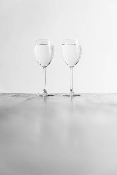 Two wine glasses filled with clear liquid on a wooden table - Φωτογραφία, εικόνα