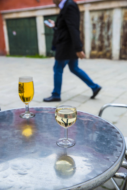 da vicino su un bicchiere di vino e di birra su un tavolino da caffè su una terrazza di caffè con una silhouette maschile che cammina sullo sfondo
  - Foto, immagini