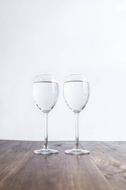 Two wine glasses filled with clear liquid on a wooden table - Photo, image