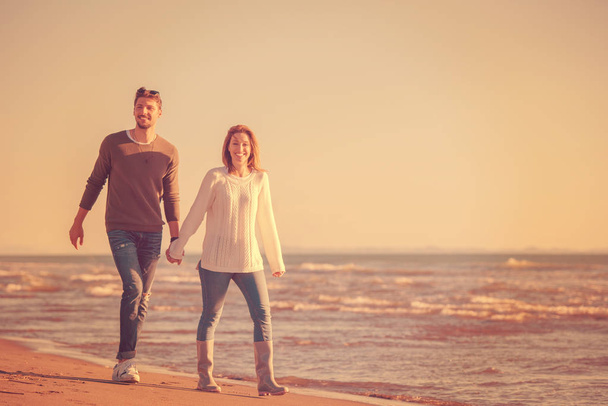 Young couple having fun walking and hugging on beach during autumn sunny day - Foto, Bild