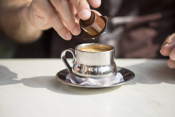 srebrna filiżanka kawy z męską dłonią nalewającą mleko śmietankowe - Zdjęcie, obraz