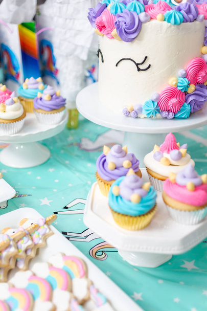 Mesa de fiesta de cumpleaños de niña pequeña con pastel de unicornio, cupcakes y galletas sugaer
. - Foto, imagen