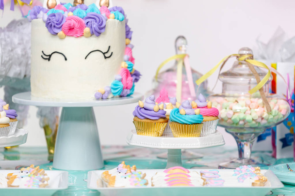 Mesa de fiesta de cumpleaños de niña pequeña con pastel de unicornio, cupcakes y galletas sugaer
. - Foto, Imagen