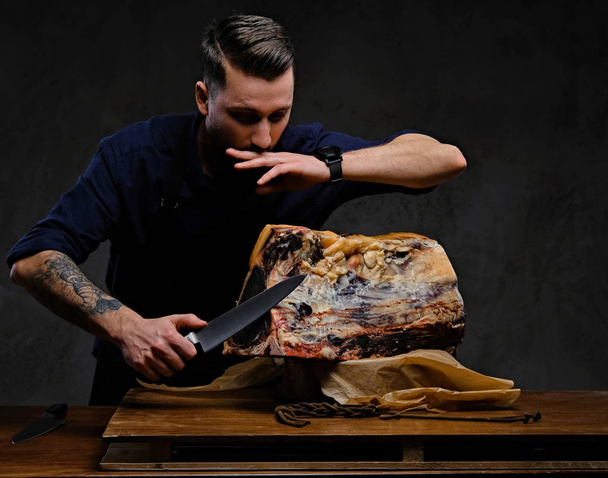 Focused chef cook cutting exclusive jerky meat on a table in a hunting house on dark background. - Foto, imagen