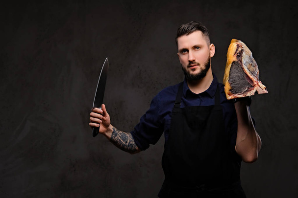 Chef cuisinier tient le couteau et un gros morceau de viande séchée exclusive sur un fond sombre
. - Photo, image