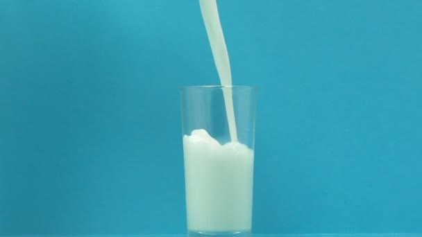 Fresh milk pouring in glass on blue background, source of calcium and phosphorus - Imágenes, Vídeo