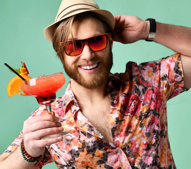 Young man in hat and sunglasses drinking margarita cocktail drink juice happy looking at camera laughing over light green - Foto, afbeelding