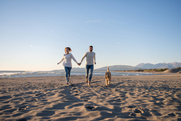 Couple Running On The Beach Holding Their Hands with dog On autmun day - Photo, image
