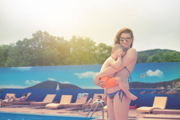 Young mom holding a baby relaxing by the pool shines the bright sun. Summer season family vacation travel - Photo, Image