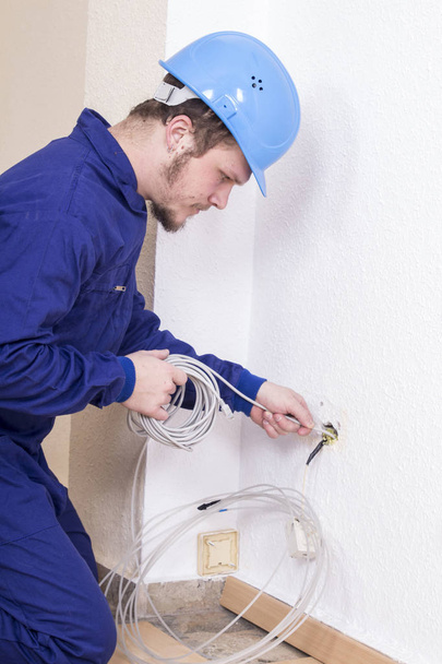 Electrician in hardhat fixing cable indoors - Photo, Image