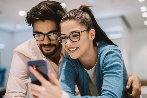 young happy couple in electronics store choosing new smartphone - Foto, Bild