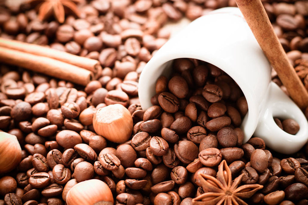 Розкидані кавові зерна з білої чашки еспресо, що лежить з паличками кориці, фундуком та зірками анісу
 - Фото, зображення
