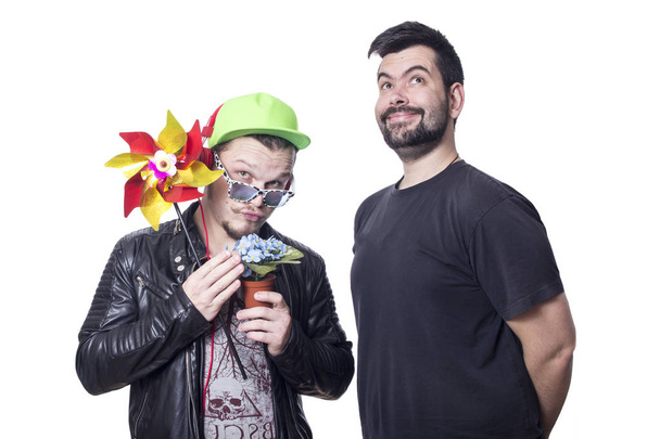 two funny men with party tools posing in studio, colorful pinwheel windmill and flowers in pot  - Foto, Imagem