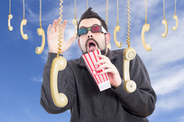 homem aterrorizado cercado por pendurar aparelhos de telefone à moda antiga vestindo óculos 3-d e segurando caixa de milho pop
 - Foto, Imagem