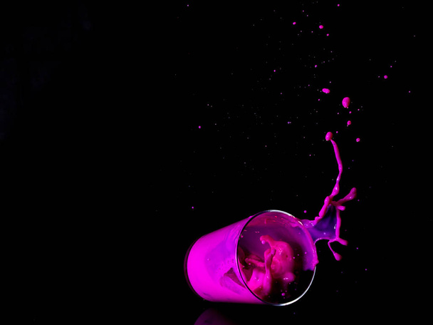 black background and falling glass with bright pink liquid - Фото, изображение