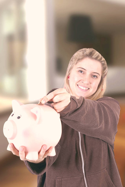 mulher loira segurando banco porquinho e olhando para a câmera
 - Foto, Imagem