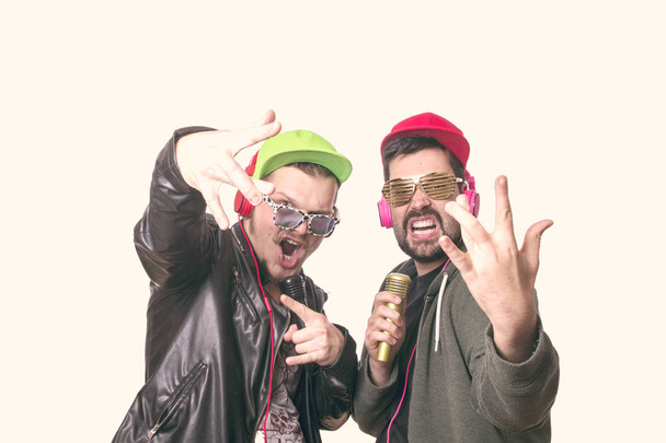 two stylish men posing in studio and wearing caps with glasses  - Photo, Image