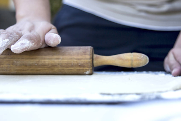 cropped image of person preparing dough at kitchen table with wooden rolling pin - Zdjęcie, obraz