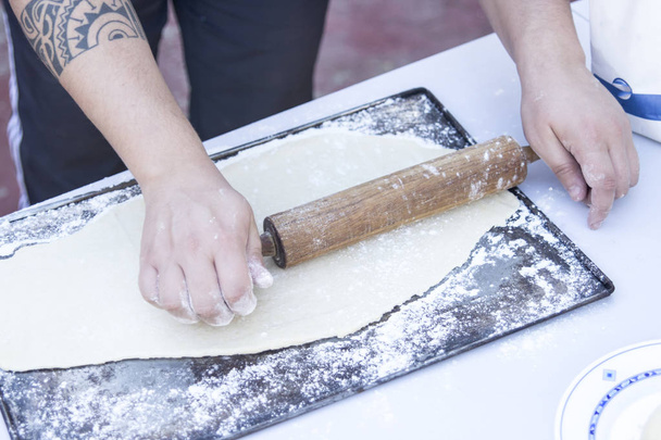 cropped image of person preparing dough at kitchen table with wooden rolling pin - Foto, afbeelding