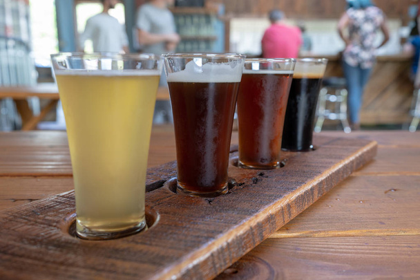 Vôo de quatro cervejas servidas em copos altos em uma bandeja de madeira
 - Foto, Imagem