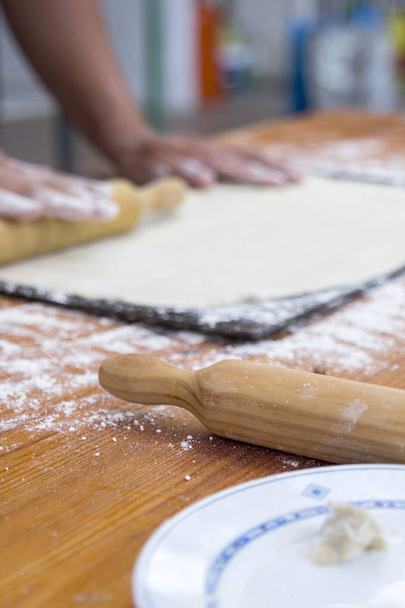 partial view of chef man hands preparing dough at kitchen with wooden rolling pin - Foto, afbeelding