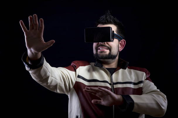 scared man wearing VR glasses in dark studio and gesturing with hands  - Fotografie, Obrázek