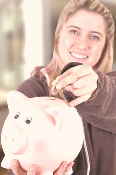 mulher loira segurando banco porquinho e olhando para a câmera
 - Foto, Imagem