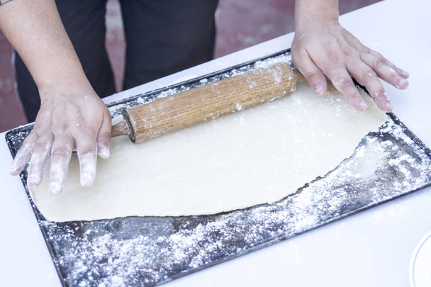 person preparing dough at kitchen table with wooden rolling pin - Фото, изображение