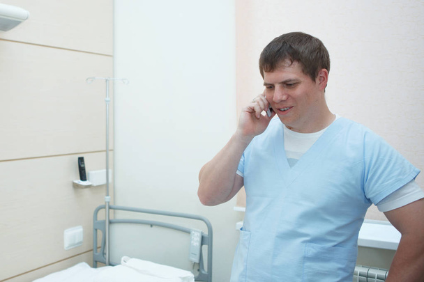 Sevimli genç cerrah hastane odasında bir smartphone konuşuyor. - Fotoğraf, Görsel
