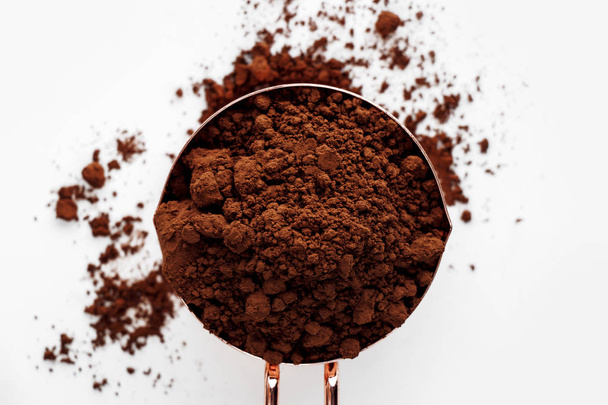 Rose gold measuring cup of cocoa powder on a white background, healthy food concept - Photo, Image