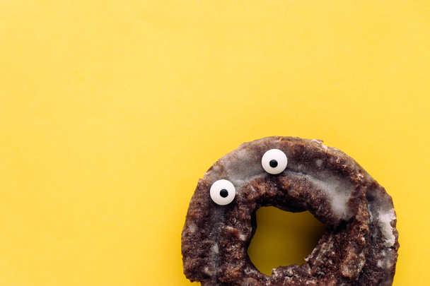 Funny shock face glazed chocolate cake donut on a pastel yellow background, creative minimal Halloween concept with copy space - Photo, Image