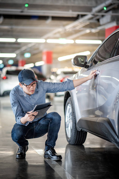 Young Asian auto mechanic holding digital tablet checking car wheel in auto service garage. Mechanical maintenance engineer working in automotive industry. Automobile servicing and repair concept - Photo, Image