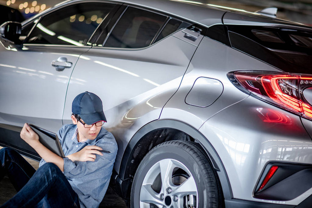 Jovem asiático auto mecânico segurando tablet digital verificando roda do carro na garagem de serviço de automóvel. Engenheiro de manutenção mecânica trabalhando na indústria automotiva. Conceito de reparação e manutenção de automóveis
 - Foto, Imagem