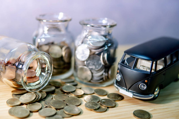 Black car model with coin in currency glass jar and spilling out on wooden table. Car loan interest rate. Saving money for auto buying. Automobile business concept - Foto, immagini