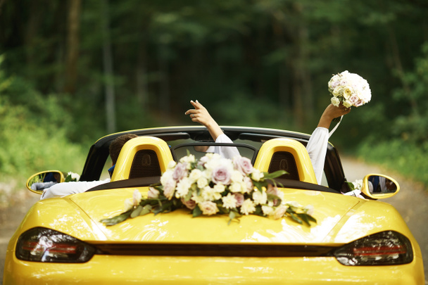 Hochzeitspaar mit Hochzeitsauto. Cabriolet. Rückseite, Braut hob die Hände mit einem Strauß. - Foto, Bild