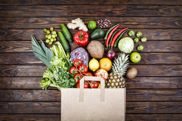 Здорове харчування. Здорова їжа в паперовій сумці макарони, овочі та фрукти на дерев'яному фоні. Концепція супермаркету вегетаріанської їжі. Вид зверху. копіювання простору
 - Фото, зображення