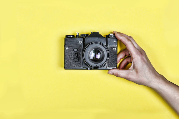 minimalismu. ženská ruka drží starý retro fotoaparát na žlutém podkladu. den, novinář. abstraktní kreativní koncept - Fotografie, Obrázek