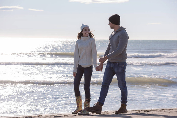 Young couple having fun walking and hugging on beach during autumn sunny day - 写真・画像
