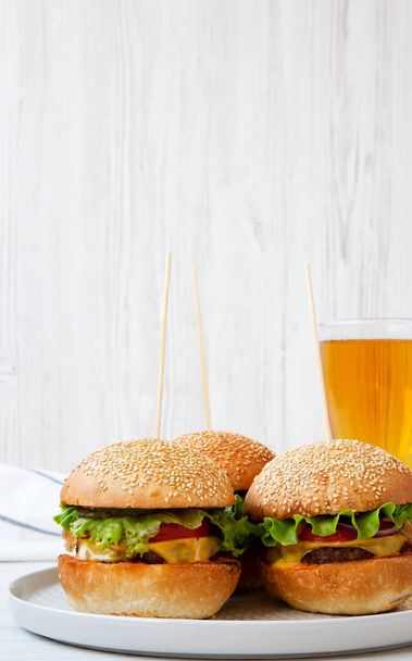 Cheeseburgery na šedou desku a sklenici piva. Bílé dřevěné pozadí. Boční pohled. Closeup. - Fotografie, Obrázek
