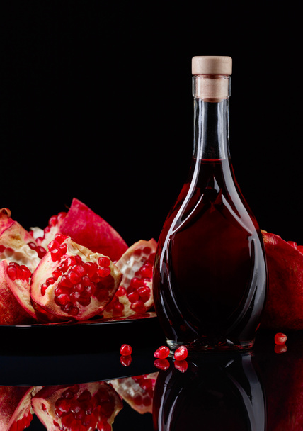reifer Granatapfel und eine Flasche Saft auf schwarzem Hintergrund - Foto, Bild