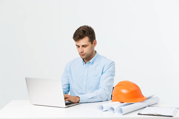 Handsome male engineer is using a notebook for work. He is sitting at the desk and smiling. Copy space on side. - Photo, Image