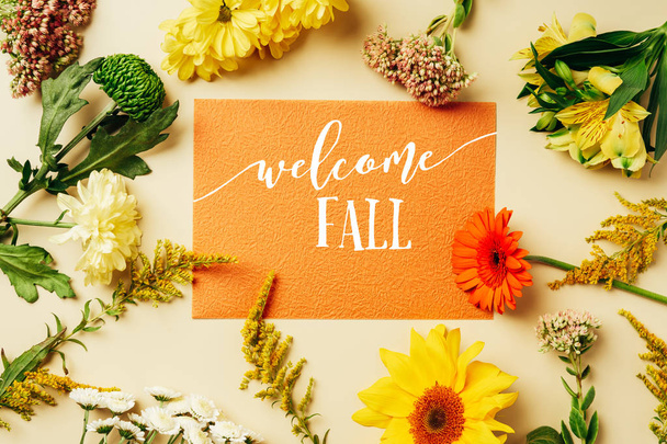 flat lay with various wildflowers around orange card with "welcome fall" lettering on beige background - Foto, afbeelding