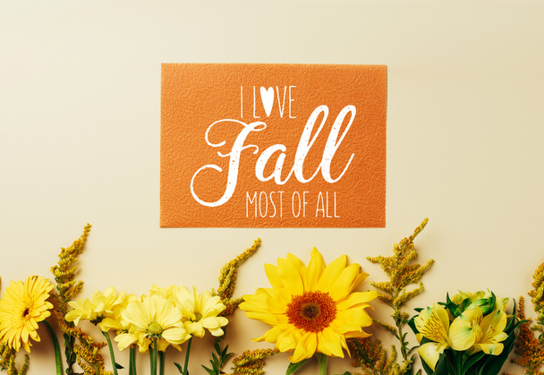 flat lay with beautiful flowers and orange card with "I love fall most of all" inspiration arrangement on beige backdrop - Photo, Image