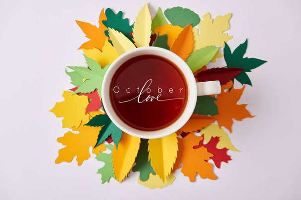 top view of cup of tea with "october love" inspiration on colorful handcrafted leaves on white surface - Photo, image