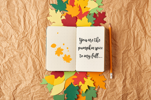 top view of notebook with "you are the pumpkin spice to my fall" lettering, pencil and colorful handcrafted paper leaves on crumpled paper background - Photo, Image