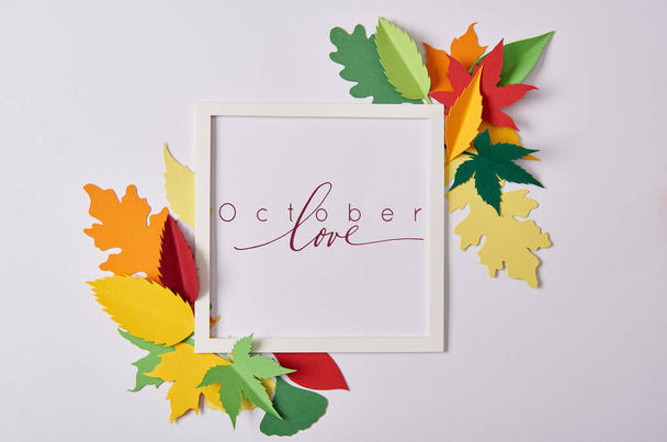 flat lay with handcrafted paper leaves and empty frame with "october love" inspiration on white tabletop - 写真・画像