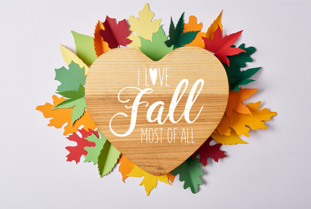 Ansicht von oben mit herzförmigem Holzbrett und bunten handgefertigten Blättern auf weißer Oberfläche mit dem Schriftzug "I love fall over all" - Foto, Bild