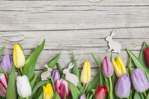 pile of fresh colorful tulips with Easter decorative bunnies on wooden background  - Фото, изображение