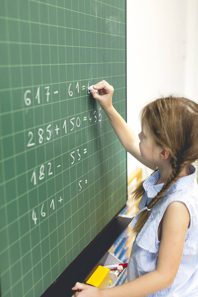 beautiful girl is counting on the blackboard in the classroom - Foto, Imagen